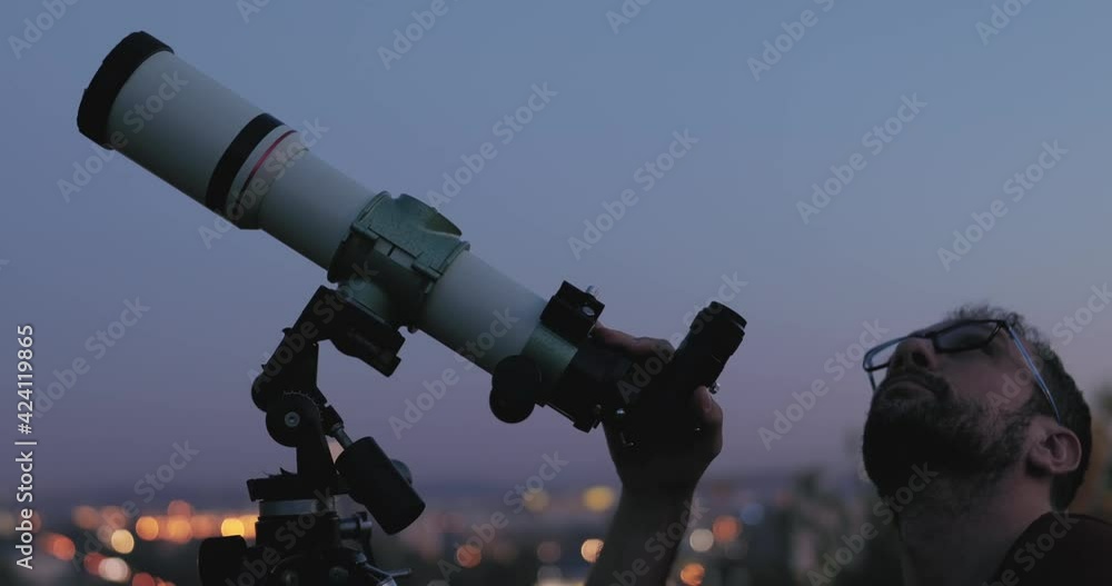 Wall mural astronomer with a telescope watching at the stars and moon with blurred city lights in the backgroun