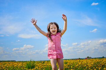 Naklejka na ściany i meble Happy small girl in a field with yellow dandelions. Female child walks in spring in nature in a sunny day