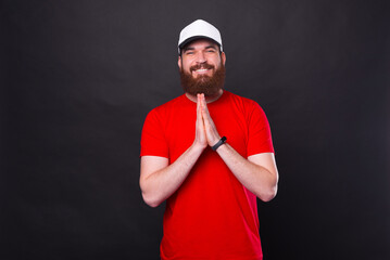 Fototapeta premium Photo of cheerful young bearded man in red t-shirt praying and gesturing