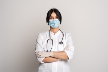 Female doctor or scientist wearing protective facial mask standing with crossed arms over grey background