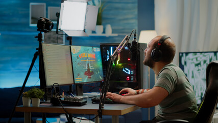 Happy streamer man winning space shooter online competition talking at professional microphone in...
