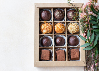 Gift craft box with assorted chocolates and pink flowers on a light concrete background. Top view.