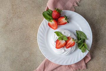 Mini Pavlova meringue cakes with strawberries and mint on a plate, concrete background. Top view.