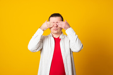 Young man closes his eyes with his hands on a yellow background.