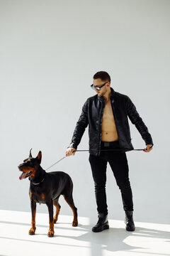 Full length body size photo of handsome guy in stylish outfit keeping doberman dog on white studio background
