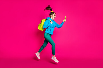Fototapeta na wymiar Full length photo of excited funky young lady wear blue sweater backpack looking modern device isolated pink color background