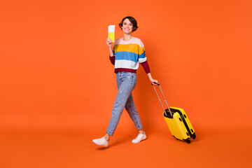 Photo of pretty sweet young woman wear wear striped sweater suitcase walking holding passport isolated orange color background