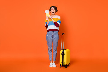 Photo of excited charming young lady dressed striped pullover luggage holding tickets isolated orange color background