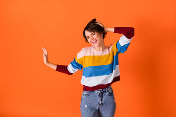 Photo of sweet charming young woman wear striped sweater dancing isolated orange color background