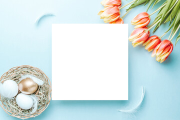 Easter basket. Golden, white colour egg in basket with spring tulips, feathers on pastel blue background in Happy Easter decoration. Foil minimalist egg design with copy space.