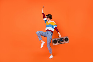 Full length portrait of cheerful cool girl arm holding recorder enjoy dance isolated on orange color background