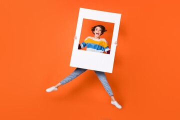 Full size photo of astonished girl jumping hands hold frame open mouth isolated on orange color...