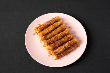 Home-baked Churro Bites on a pink plate on a black background, side view.