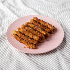 Home-baked Churro Bites on a pink plate on cloth, low angle view.