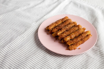 Home-baked Churro Bites on a pink plate on cloth, side view. Copy space.