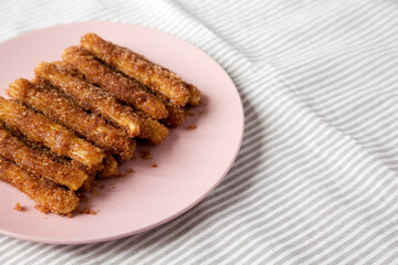 Home-baked Churro Bites on a pink plate on cloth, low angle view. Space for text.