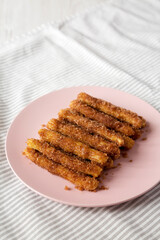 Home-baked Churro Bites on a pink plate on cloth, low angle view. Copy space.