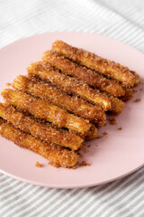 Home-baked Churro Bites on a pink plate on cloth, side view. Close-up.