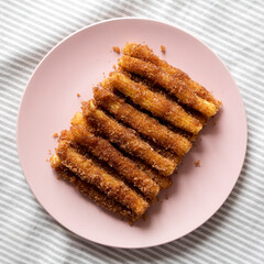 Home-baked Churro Bites on a pink plate on cloth, overhead view. Flat lay, top view, from above.