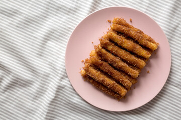 Home-baked Churro Bites on a pink plate on cloth, top view. Flat lay, overhead, from above. Space for text.