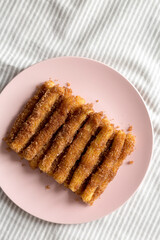 Home-baked Churro Bites on a pink plate on cloth, top view. Flat lay, overhead, from above. Copy space.