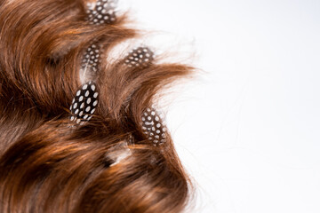 Naklejka premium Multicolored feathers are woven into dark brown hair on a white background