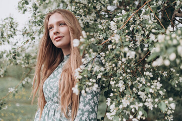 a beautiful girl with long brown hair in a green dress stands in the blooming apple trees