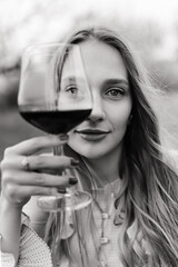 a beautiful girl with brown hair in a beige dress holds a glass of red wine in her hand in a blooming apple orchard