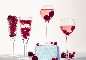 Fototapeta na wymiar transparent glasses of pink gin infused with cranberry on light background, crystal glasses of spirits drinks with berries, a row of cherry liquor or any red alcoholic cocktail, minimalism