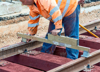 construction of railway track with wooden sleepers. Worker with a drill makes the hole in which the bolt that holds the rail fixed on the sleeper will be fixed.