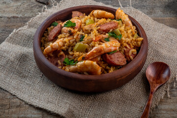 Jambalaya with shrimps and sausages on a wooden background.