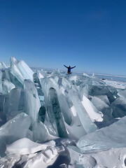 Fototapeta na wymiar Happy tourist sits on the ice troughs of Lake Baikal. Large, impenetrable chunks of ice.