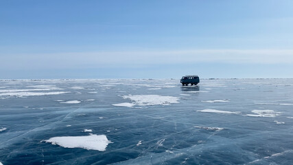 People travel on the ice of frozen Lake Baikal in a Soviet car. Transparent blue ice with deep unique cracks