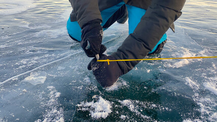 Tourist screws an ice screw into the ice. Frozen Lake Baikal. Winter hike.