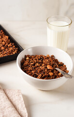 Homemade chocolate granola in a white plate with milk on a light background. Healthy breakfast