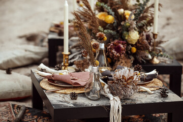 A table  designed for a boho style event with an eucalyptus, vintage plates and other rustic touches. On seaside in the sand