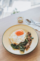 Thai food (Stir Fried Basil, Pork, Fried Egg), Stir Fried Basil with Minced Pork, Fried Egg, Topped on Steamed Rice in a Zinc Plate on a Wooden Table