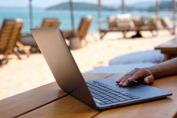 Closeup of a woman working and touching on laptop touchpad on the beach
