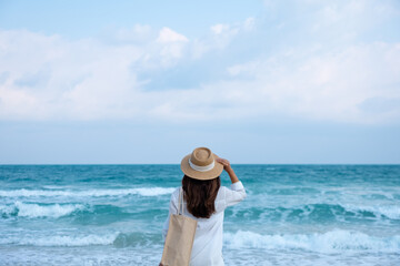 Rear view image of a woman with hat and bag looking at the sea with blue sky background