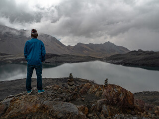 Guy person looking in a moody landscape with lake, ice, snow and clouds in nevado pastoruri, huaraz, peru