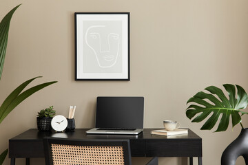Stylish composition of home office interior with black wooden desk, chair, tropical flower in vase, laptop, mock up poster frame, cup of coffee, clock and elegant office accessories. Template.