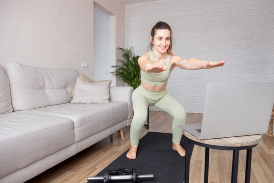 Fit woman athlete in sportswear repeating after coach making squats during online fitness workout on mat at home. Active healthy lifestyle, training at home and online training concept.
