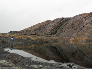 Moody landscape of mountains and lagoon with person looking at reflection in Nevado Pastoruri, Huaraz, Peru	