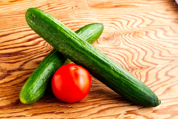 two cucumbers and a tomato on a wooden surface