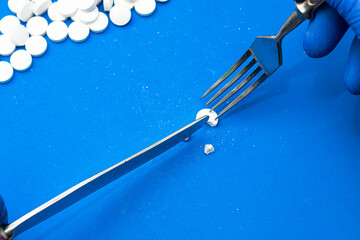a man wearing blue medical gloves eats pills with a knife and fork