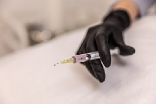 Doctor's hand in black glove with syringe.