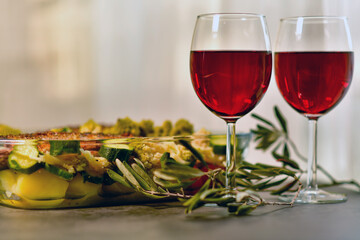 two glasses of red wine and a large glass dish with baked fish and vegetables
