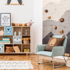 Stylish scandinavian interior design of childroom with gray sofa, modern climbing wall for kids, design furnitures, soft toys, teddy bear and cute children's accessories. Home decor. Template. 
