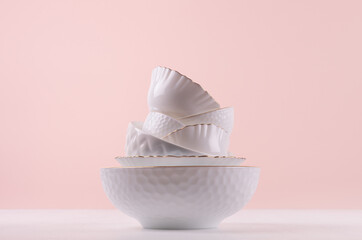 White ceramic crockery stack with golden bezel, different texture on white wooden table, pastel pink wall, elegant delicate kitchen interior.