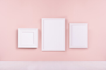 Elegant simple modern gallery with set of three blank different photo frame hanging on pastel pink wall and white wood floor. Mock up for portfolio, design or text.